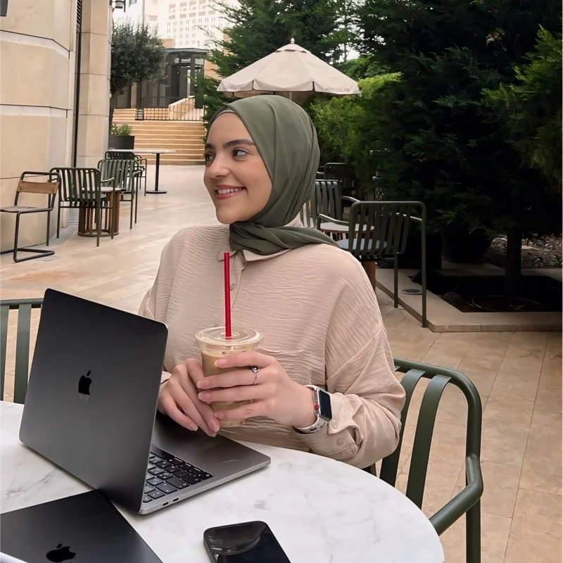 Aya Almomany smiling at a café table with her MacBook